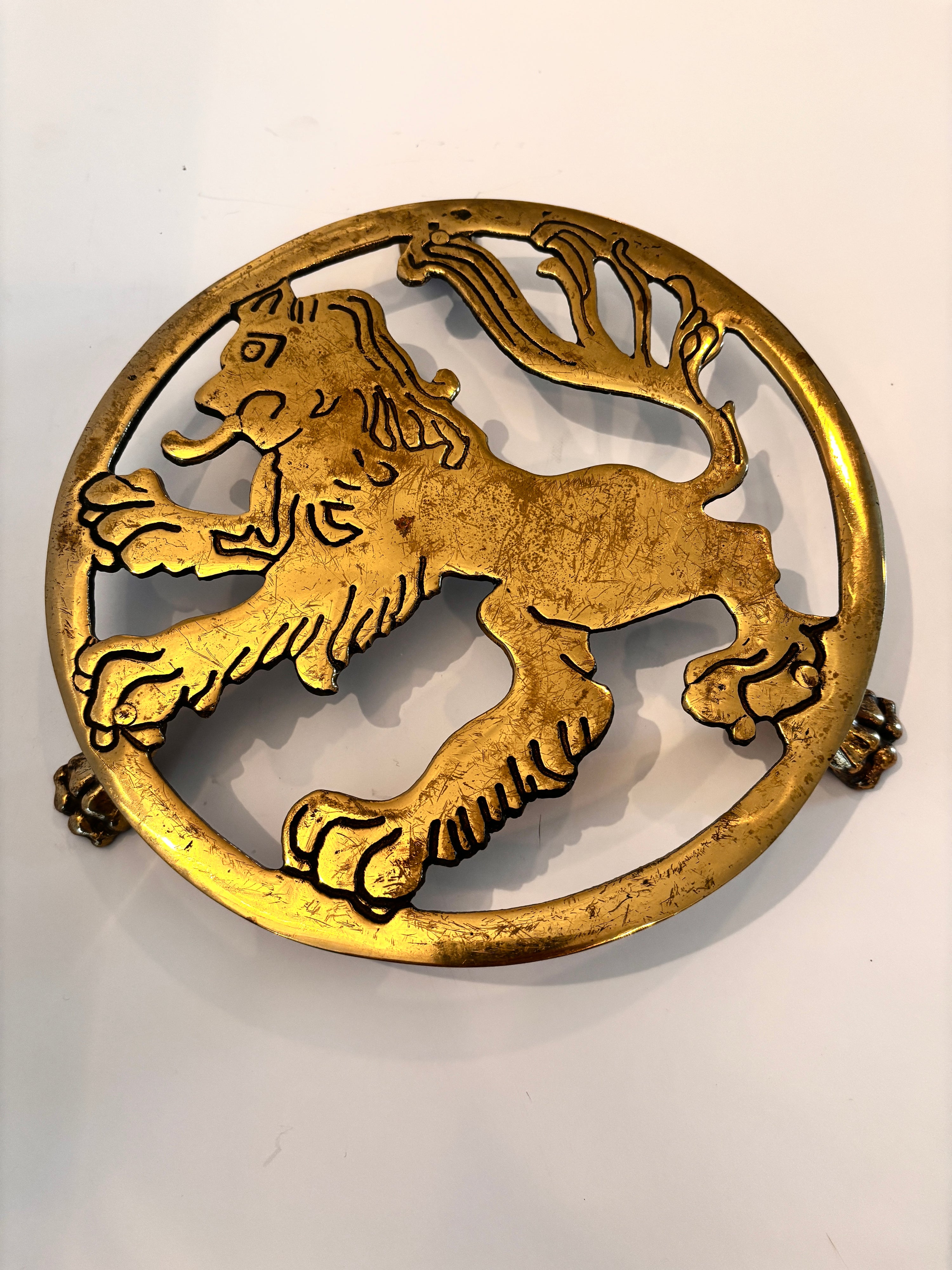 Vintage English brass trivet with a lion motif in a circular frame on clawfoot supports, 7.5 inches
