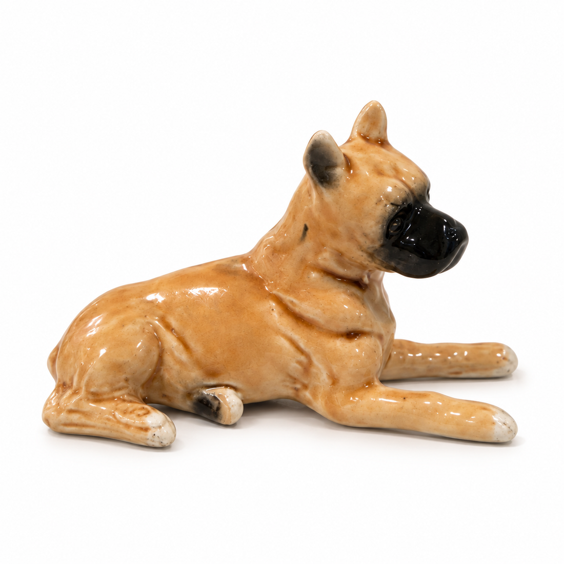Vintage hand-painted fawn porcelain boxer dog figurine lying down, 2 inches tall, on a white background