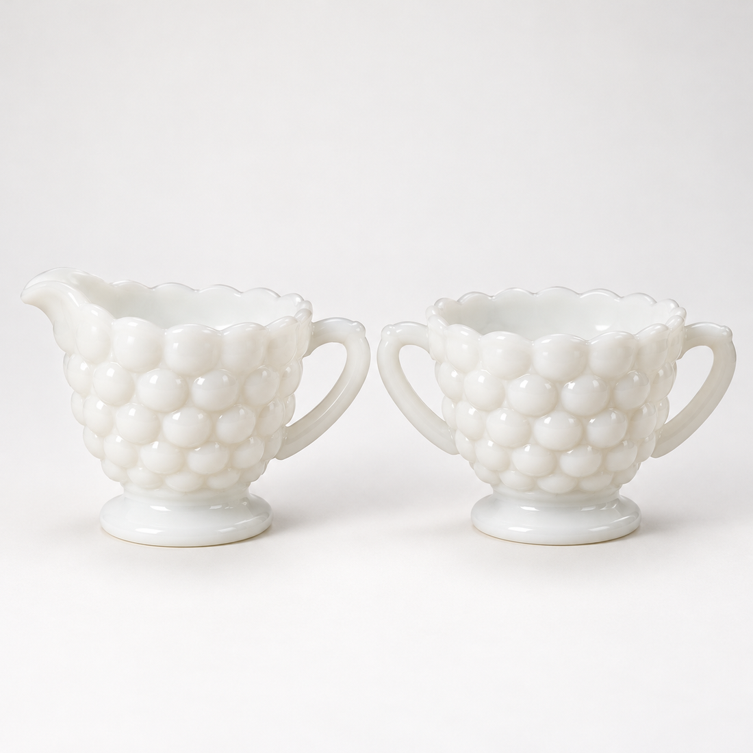 Vintage white milk glass creamer and sugar bowl set with raised bubble pattern and footed bases, on a white background
