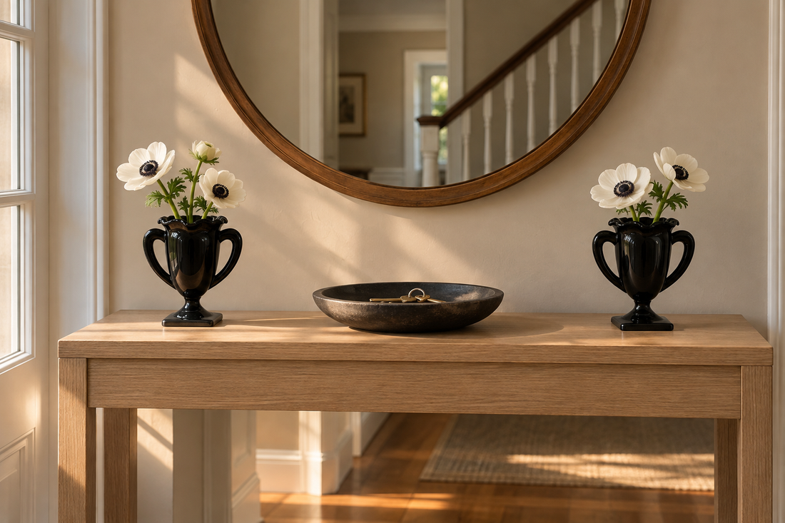 Pair of L.E. Smith black amethyst glass trophy vases with white anemones at either end of a pale oak front hall console under a round mirror