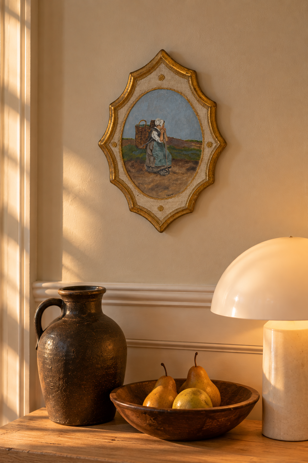Patti McCarthy oil of a woman with a wicker basket on a shaped gilt Florentine board, hung on a warm wall above an oak console with a stoneware jug, pears and a mushroom lamp