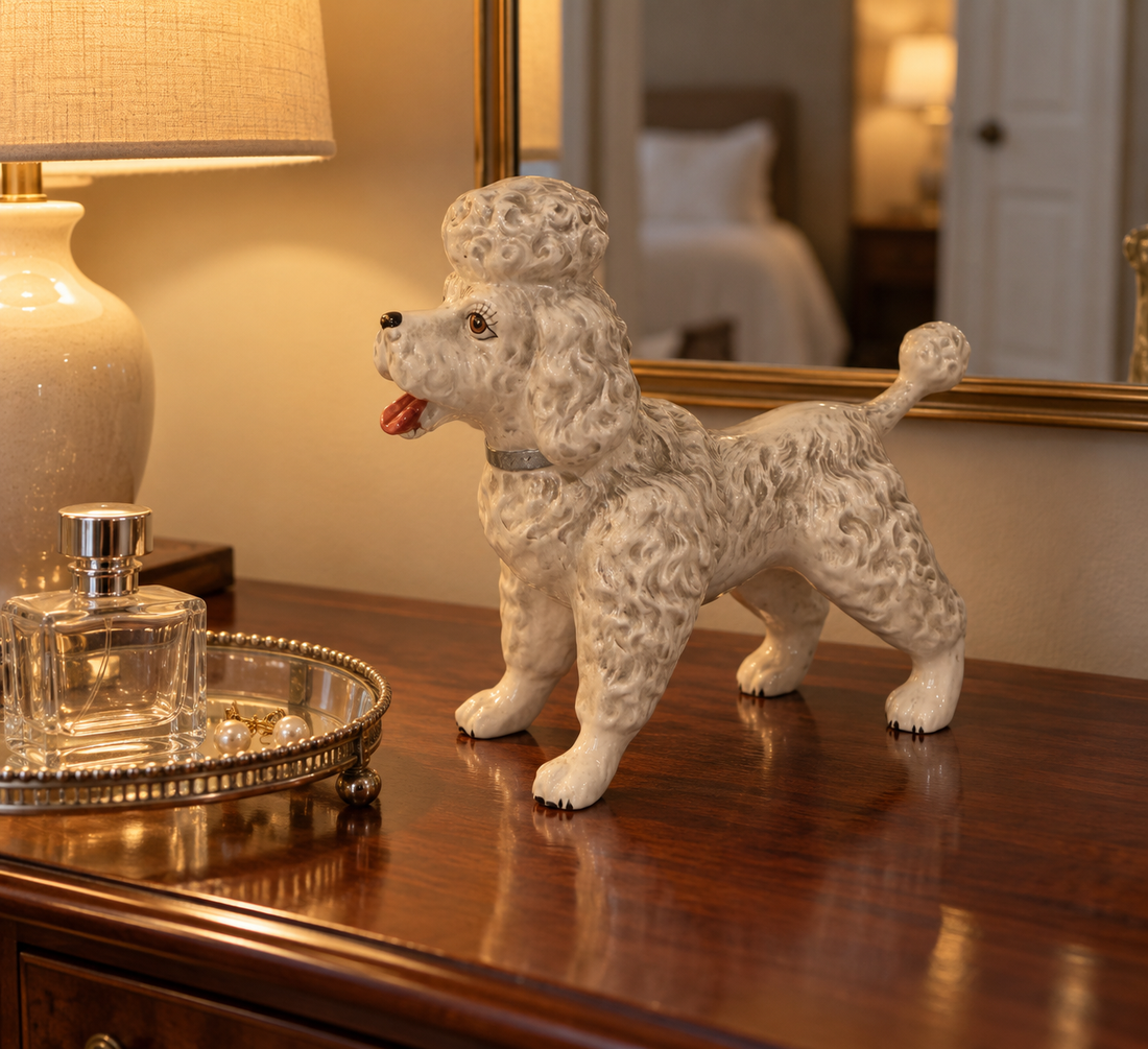 Norcrest white porcelain poodle figurine on a mahogany chest beside a glass perfume tray in a lamplit bedroom