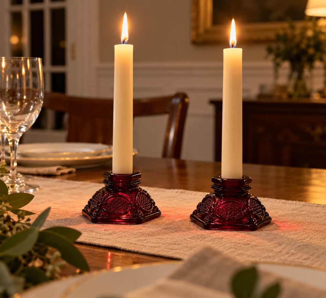 Pair of ruby red Cape Cod glass candleholders with lit ivory tapers on a linen runner on a dining table set for dinner