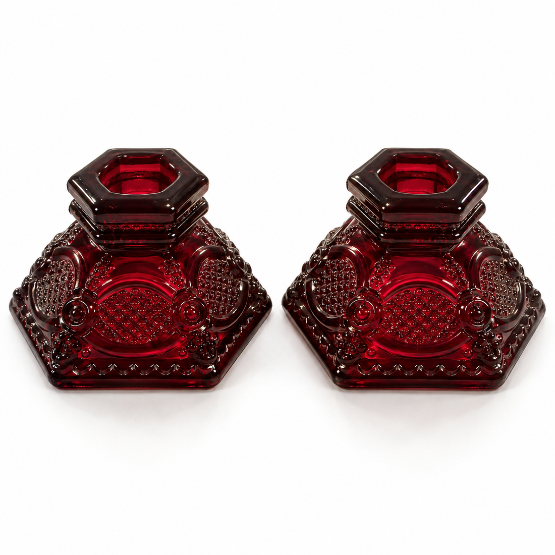 Pair of Avon Cape Cod ruby red pressed glass candleholders with hexagonal bases, 2 inches tall, on a white background
