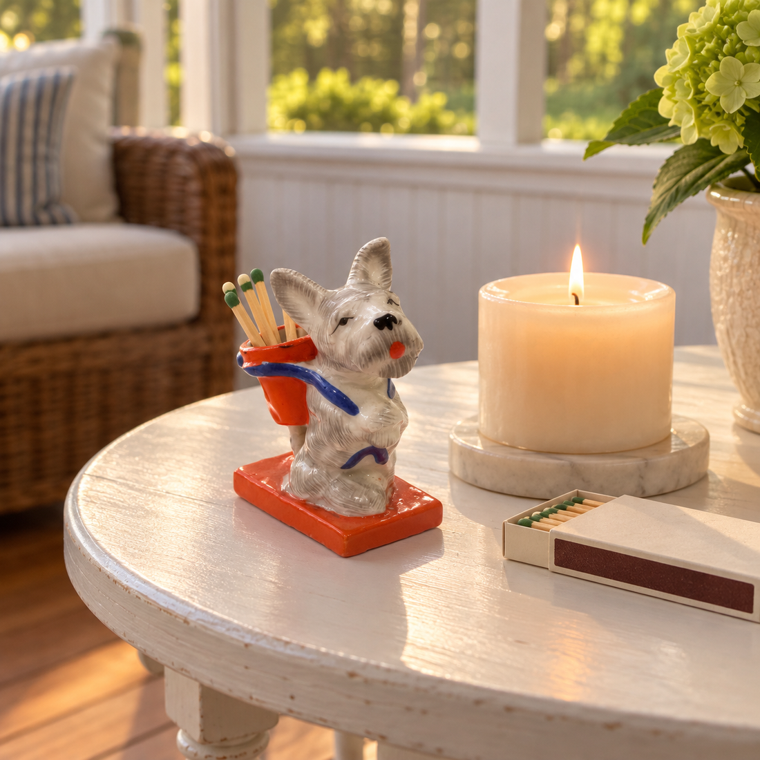 Vintage porcelain Scottie dog match holder with wooden matches on a white porch side table beside a lit candle