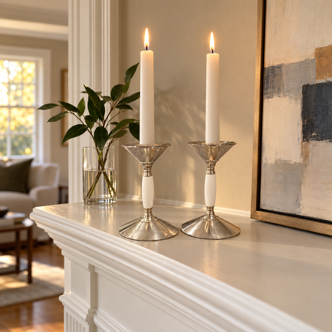 Pair of silver plated candleholders with white stems and white tapers on a painted mantel